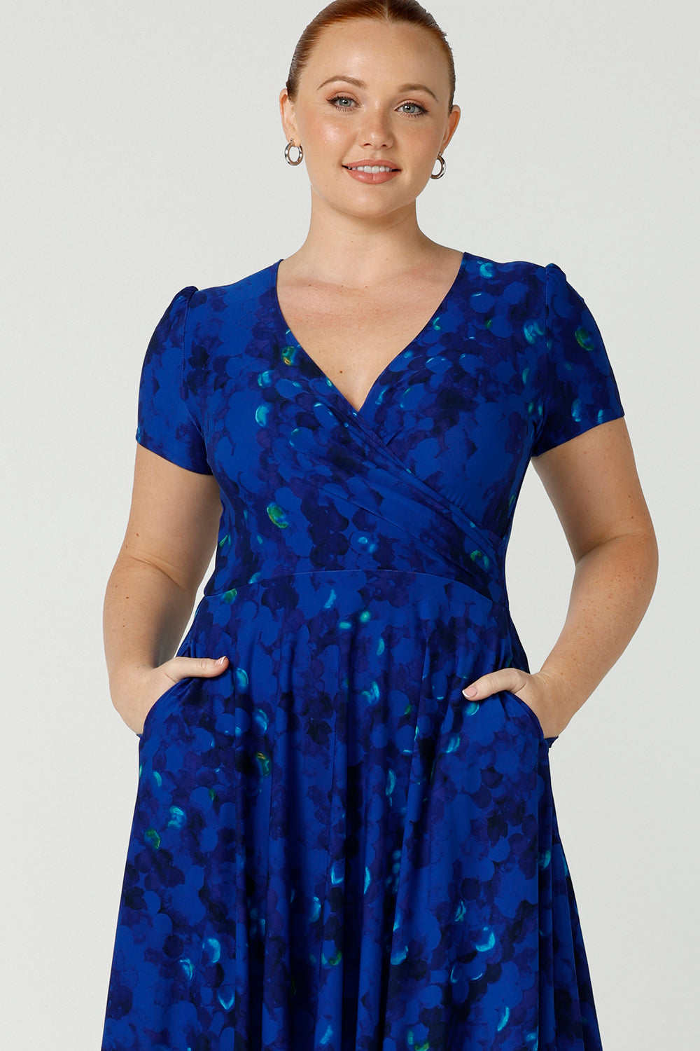 A size 12 fuller figure woman, wearing a chic dress for plus size and fuller figure women, this V-neck dress with 3/4 sleeves comes in a cobalt abstract spotted print and has a knee-length skirt, this dress is good for casual weekend wear.’