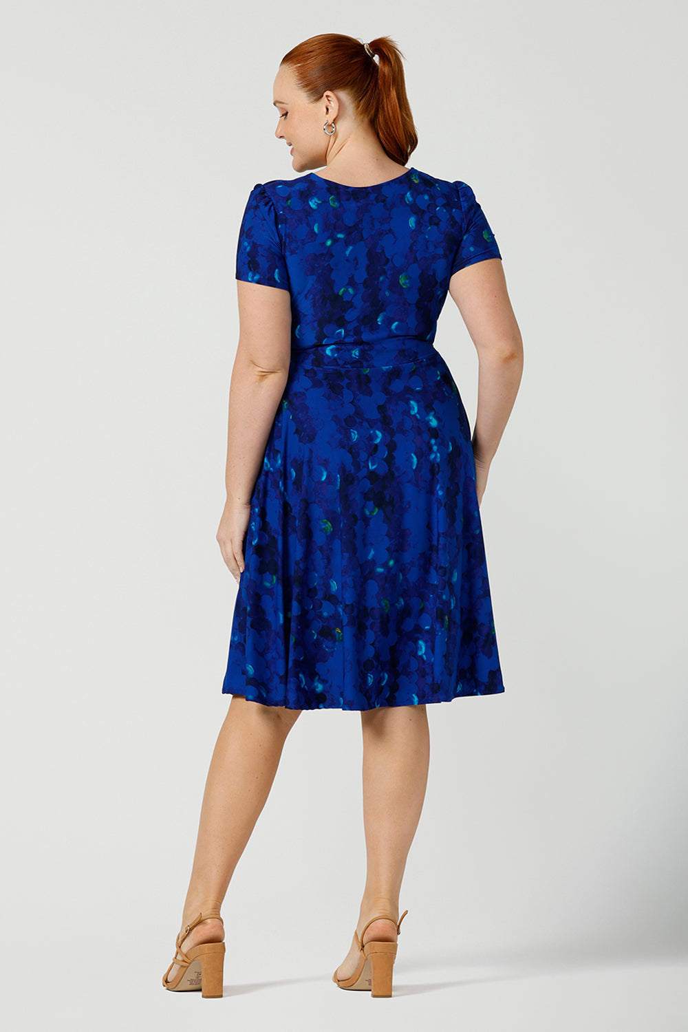 Back view of a size 12 fuller figure woman, wearing a chic dress for plus size and fuller figure women, this V-neck dress with 3/4 sleeves comes in a cobalt abstract spotted print and has a knee-length skirt, this dress is good for casual weekend wear.