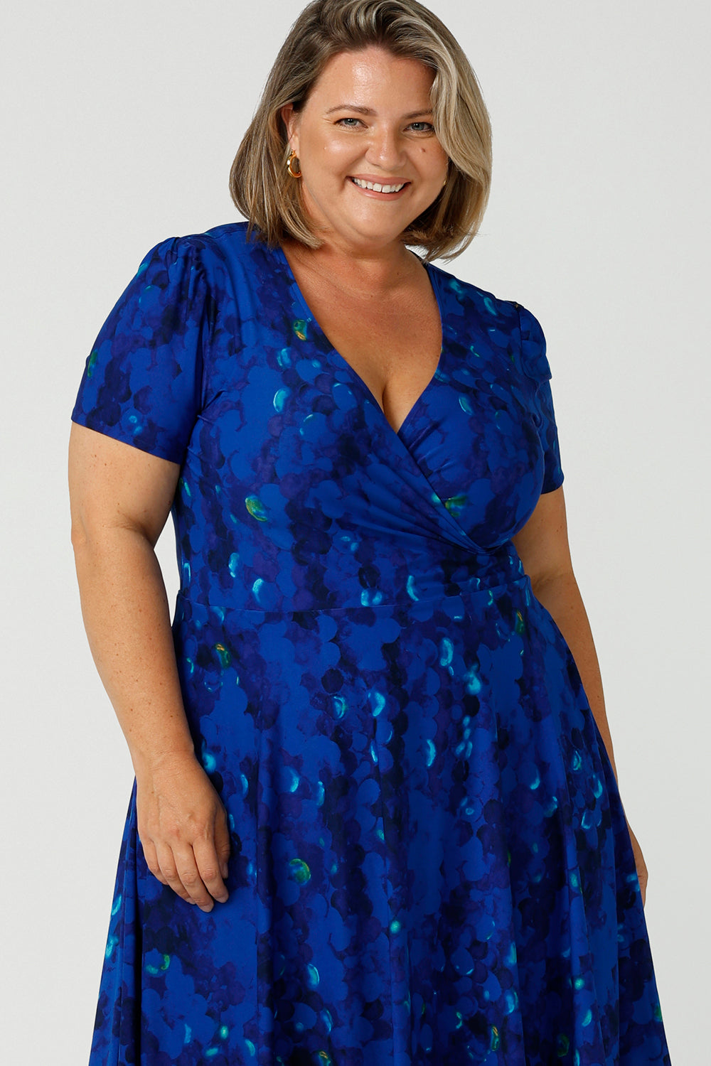 Close up of the neckline of a plus size 18 woman, wearing a chic dress for plus size and fuller figure women, this V-neck dress with 3/4 sleeves comes in a cobalt abstract spotted print and has a knee-length skirt, this dress is good for casual weekend wear.