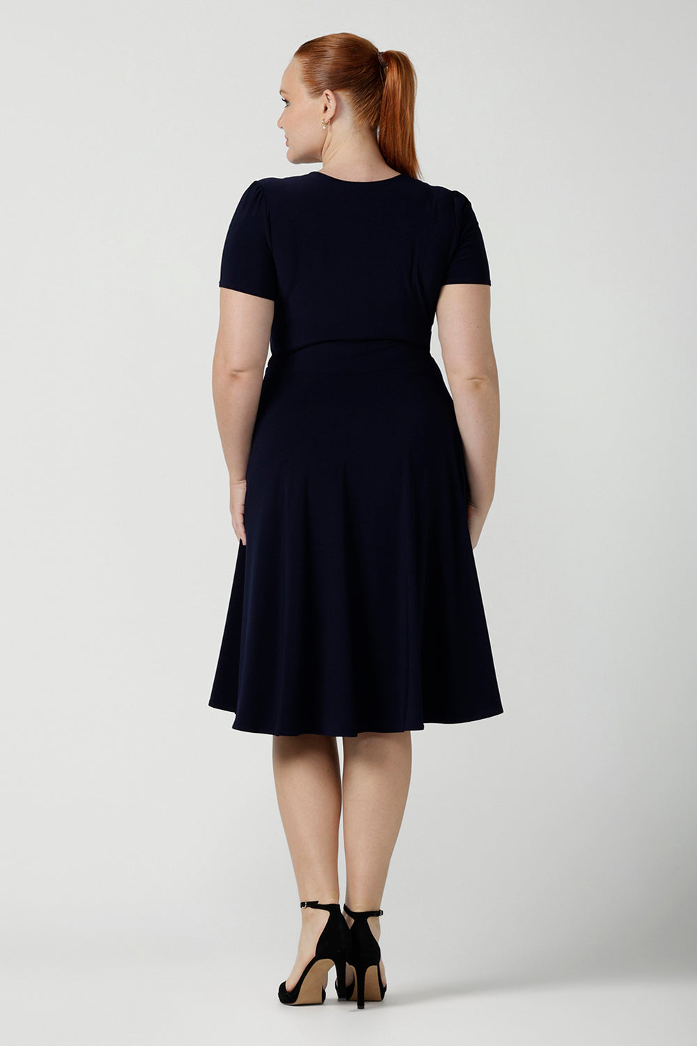Back view of a fixed Wrap Bibi dress in Navy. Curvy size 12 woman wears a jersey dress the perfect corporate comfortable work dress. Below the knee length. Size 8 - 24.