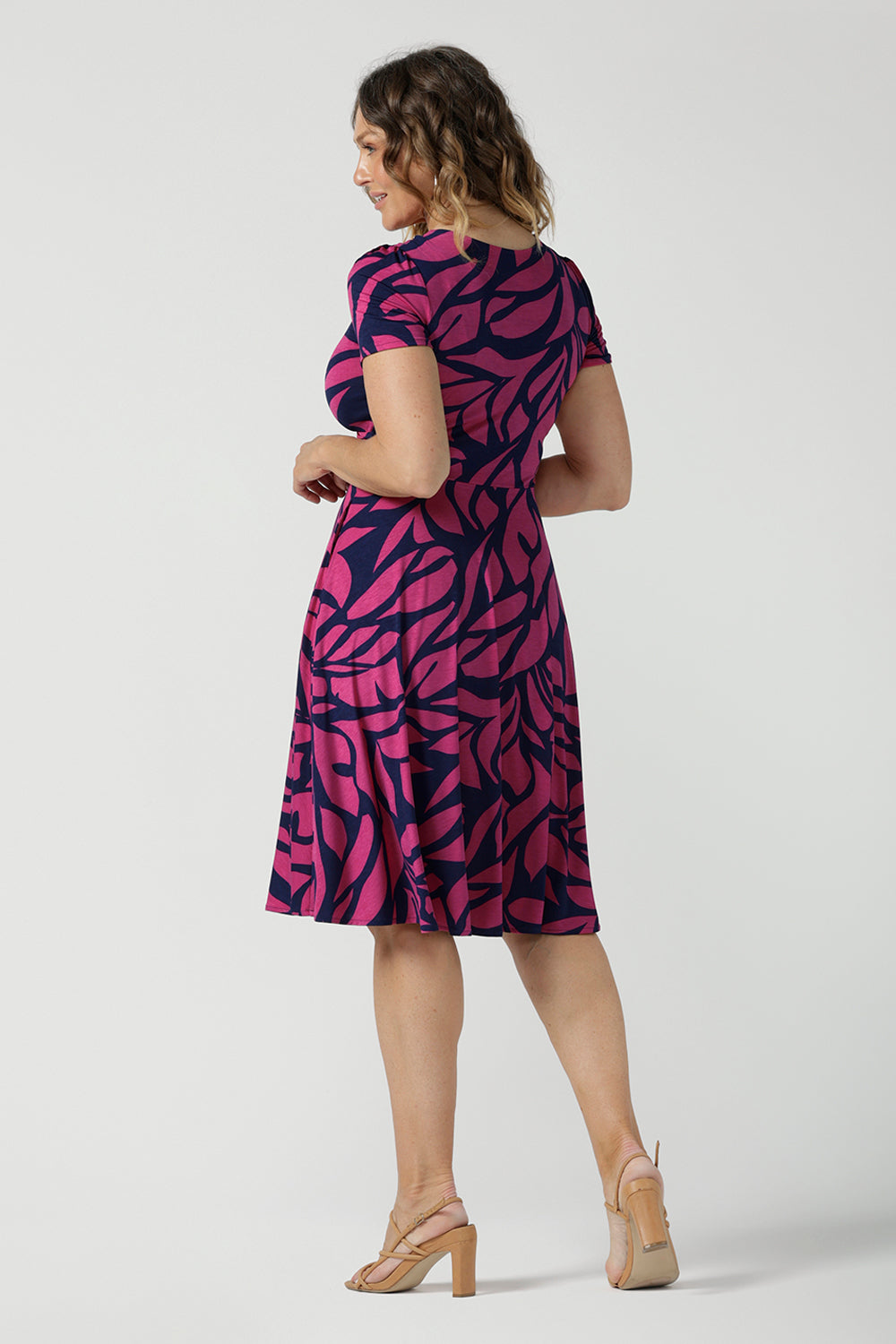 Back view of a Bibi Fixed Wrap Dress in Pink Jungle. A pink and navy abstract print dress made in comfortable jersey fabric. Just below knee length with short sleeves. A v-neeckline. Designed for petite to plus size women -24. Designed and made in Australia. 