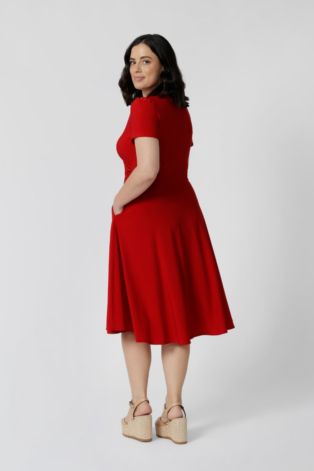 Back view of petite model wears knee length red dress. Sleeved dress is made from soft dry touch jersey fabric. This red dress has been designed with comfortability and style in mind. Knee length dress is perfect for festive season with its beautiful red standout colour. Leina & Fleur stocks Bibi Dresses in sizes 8-24 including both petite and plus sizes 