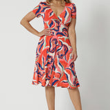 The best fixed wrap dress for over 50s women, the Bibi Wrap Dress is new in Tangerine, Red, White, Mint Green and Purple retro print. Shown on a size 12 woman, this summer wrap dress is a fit and flare style with full, knee length skirt and pockets. Easy-care, it's a good dress for travel and cruise wear. Made in Australia by Australian and New Zealand women's clothes brand Leina & Fleur.