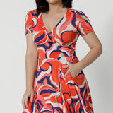 Close up of a good fixed wrap dress for petite height women, the Bibi Wrap Dress is new in Tangerine, Red, White, Mint Green and Purple retro print. Shown on a petite woman, this summer wrap dress is a fit and flare style with full, knee length skirt and pockets. Easy-care, it's a good dress for travel and cruise wear. Made in Australia by jersey wrap dress specialists, Australian and New Zealand women's clothes brand Leina & Fleur.