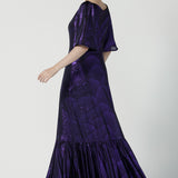 Back view of a size 10 woman wears a glamorous maxi dress with a ruffle hem and low v-neckline. Featuring a flutter sleeve and made in shiny purple jersey with a foil print. Made in Australia for women for evening gown cocktail wear. Size 8 - 24.