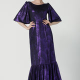 A size 10 woman wears a glamorous maxi dress with a ruffle hem and low v-neckline. Featuring a flutter sleeve and made in shiny purple jersey with a foil print. Made in Australia for women for evening gown cocktail wear. Size 8 - 24.