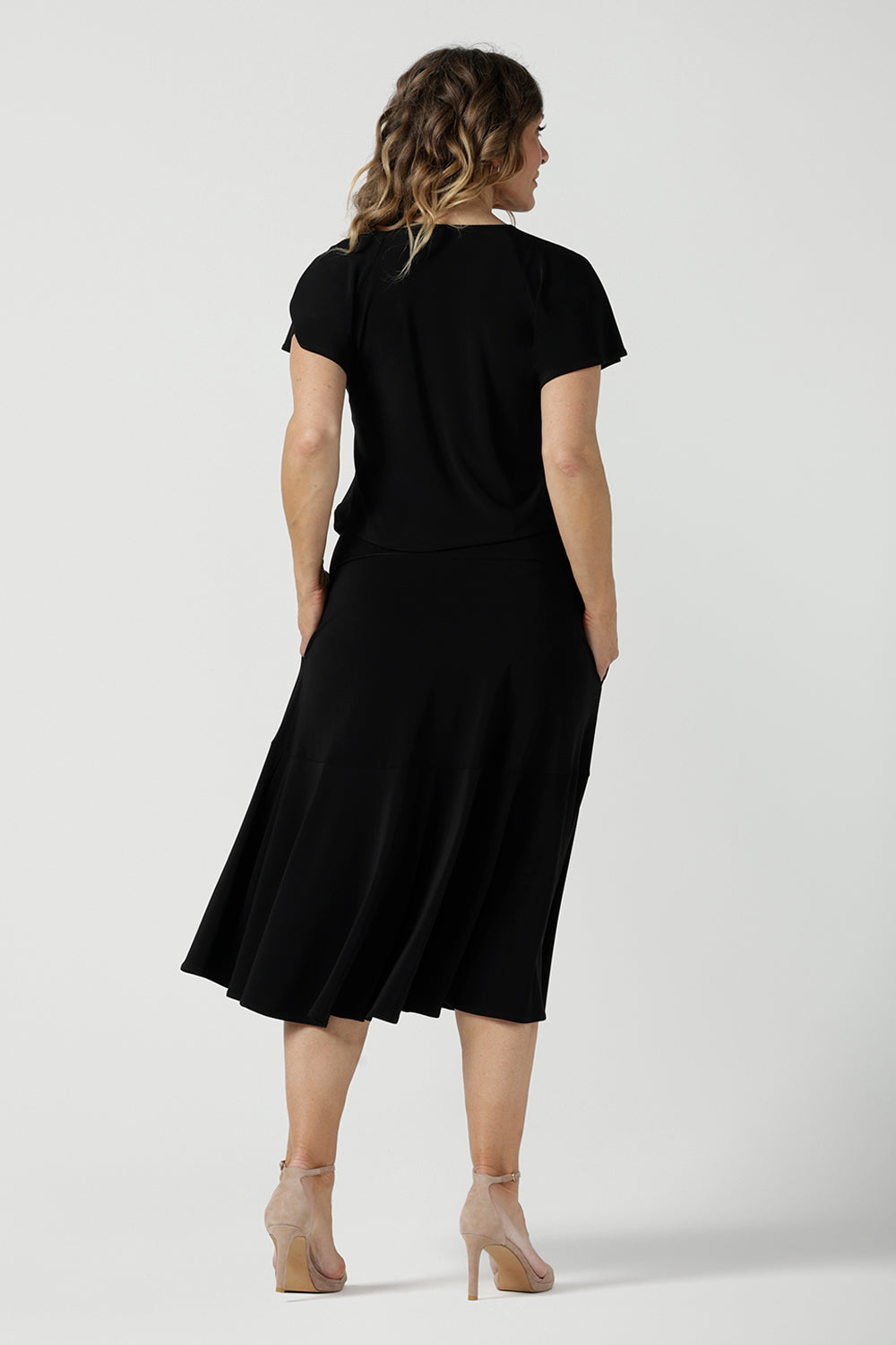 Back view of a size 10 woman wears the Bowie Top in Black. A jersey flutter sleeve style with a v-neckline and tie neck. Made in Australia for women 8-24.