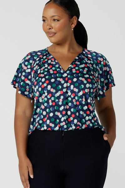 Curvy woman in a size 16 wears a Bowie top with a flutter sleeve  and v-neck with neck ties. All over polka dot print on a soft slinky jersey. Comfortable work top for women. Made in Australia size 8 - 24.