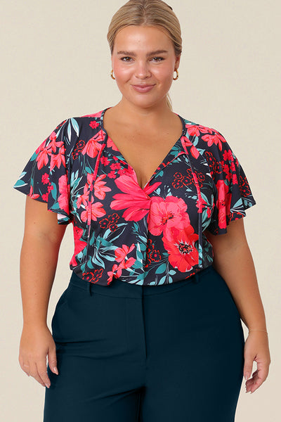 A plus size, size 14 woman wears a casual jersey top. The top has short raglan sleeves, a V-neckline and is printed with a floral pattern for a casual weekend look.