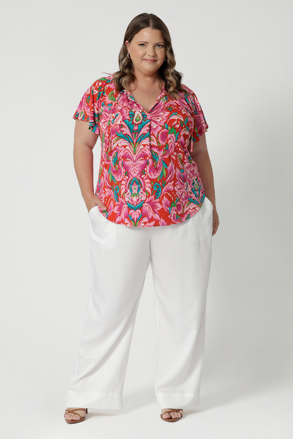 Plus sized model wears flattering V-neck top with delicate thin ties that can be adjusted for a customisable fit. Easy care fabric is on a tropical abstract print, made from lightweight crepe jersey. Providing breathability and comfortability. Shop this ideal summer top in sizes 8-24. 