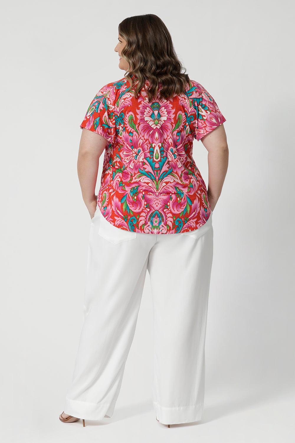 Back view of plus sized wearing summer ready top with shirttail hemline that can be adjusted for a customisable fit. Easy care fabric is on a tropical abstract print, made from lightweight crepe jersey. Shop this breathable and comfortable summer top in sizes 8-24. 