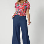 Flutter sleeved summer top offers a relaxed fit that drapes beautifully with v neck and shirt tail hemline features. Ideal piece for staying cool and stylish during the summer months. Model pairs printed blouse with denim pants to create a casual day look. This top is comes in sizes 8-24, made by Leina & Fleur