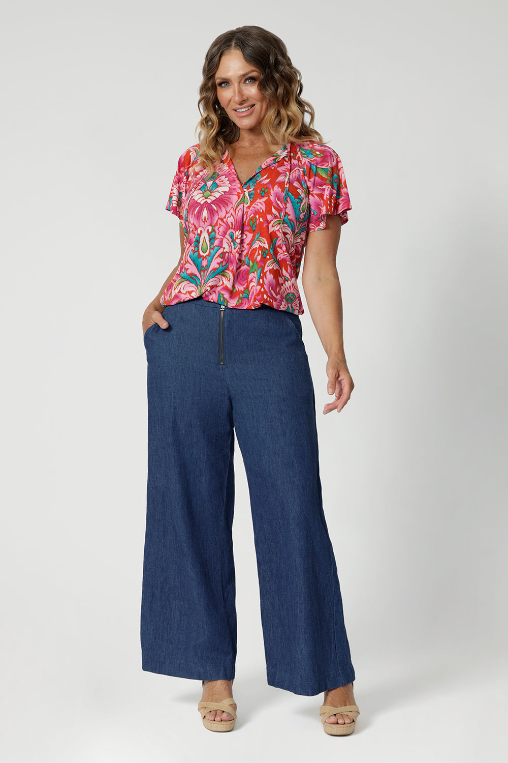 Flutter sleeved summer top offers a relaxed fit that drapes beautifully with v neck and shirt tail hemline features. Ideal piece for staying cool and stylish during the summer months. Model pairs printed blouse with denim pants to create a casual day look. This top is comes in sizes 8-24, made by Leina & Fleur