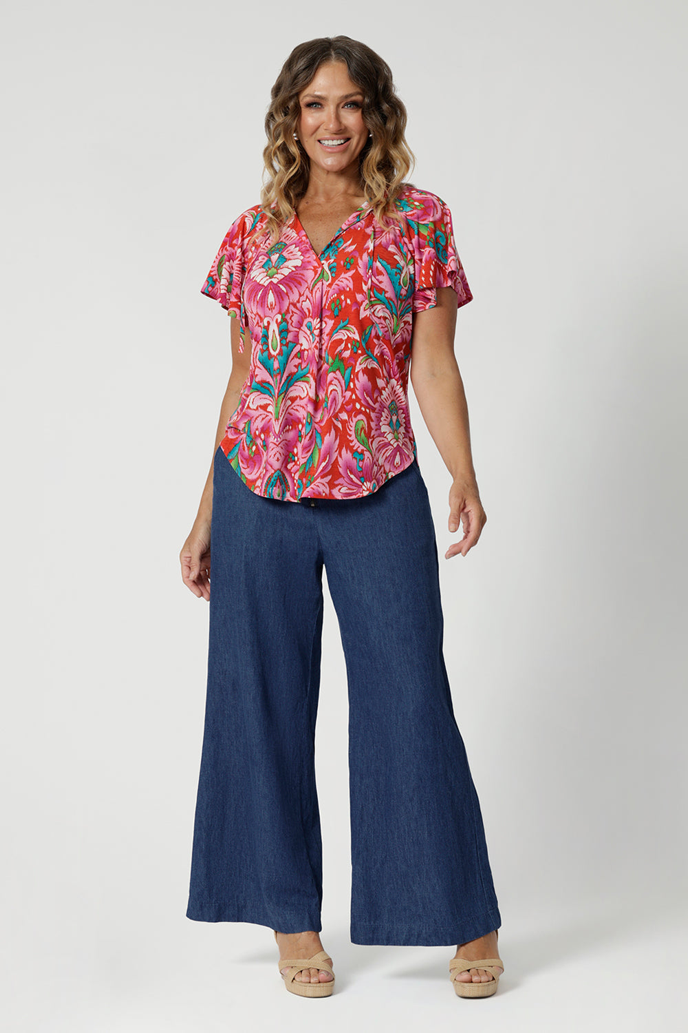 Flutter sleeved top made from breathable jersey crepe fabric is a summer staple.  Offering a relaxed fit that drapes beautifully with v neck and shirt tail hemline features. It's the ideal piece for staying cool and stylish during the summer months. Model pairs printed blouse with denim pants to style a casual ensemble. 