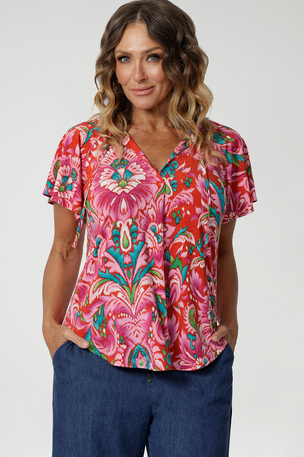 Close up image of 40 year old woman wears flutter sleeved summer printed blouse, featuring v neckline, shirt tail hemline & short flutter sleeves. Made from easy care and lightweight crepe jersey, that is breathable and comfortable. Leina & Fleur proudly stock petite and plus sizes 8-24.