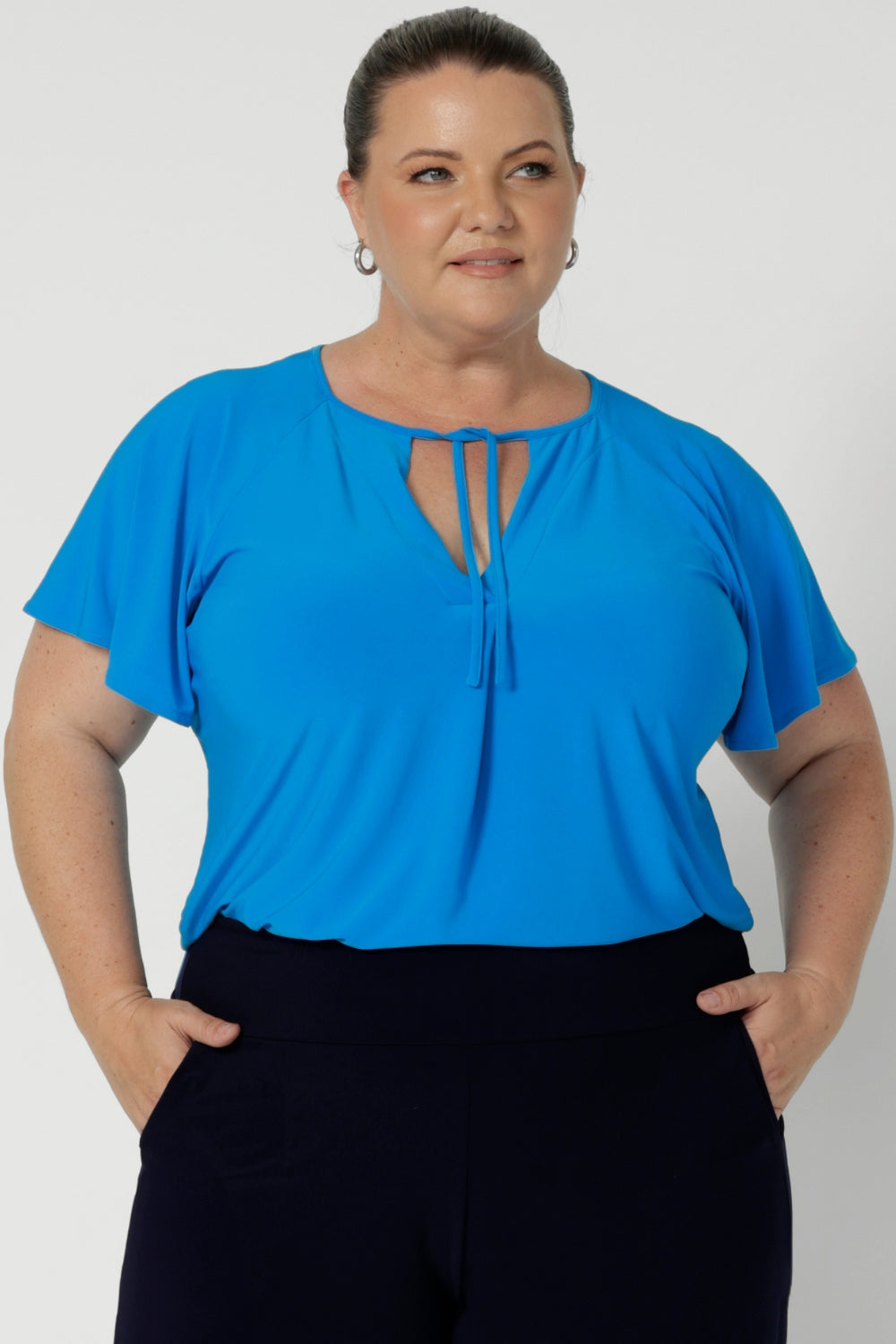 The relaxed fit offers a comfortable and slightly loose drape, while the V-neckline with thin fabric ties allows for customisation. Either left undone for a more casual feel or tied in the front for a chic, polished look. A center front pleat adds structure and subtle detail, enhancing the flattering shape of the top. Workwear top is now available in size 8-24.