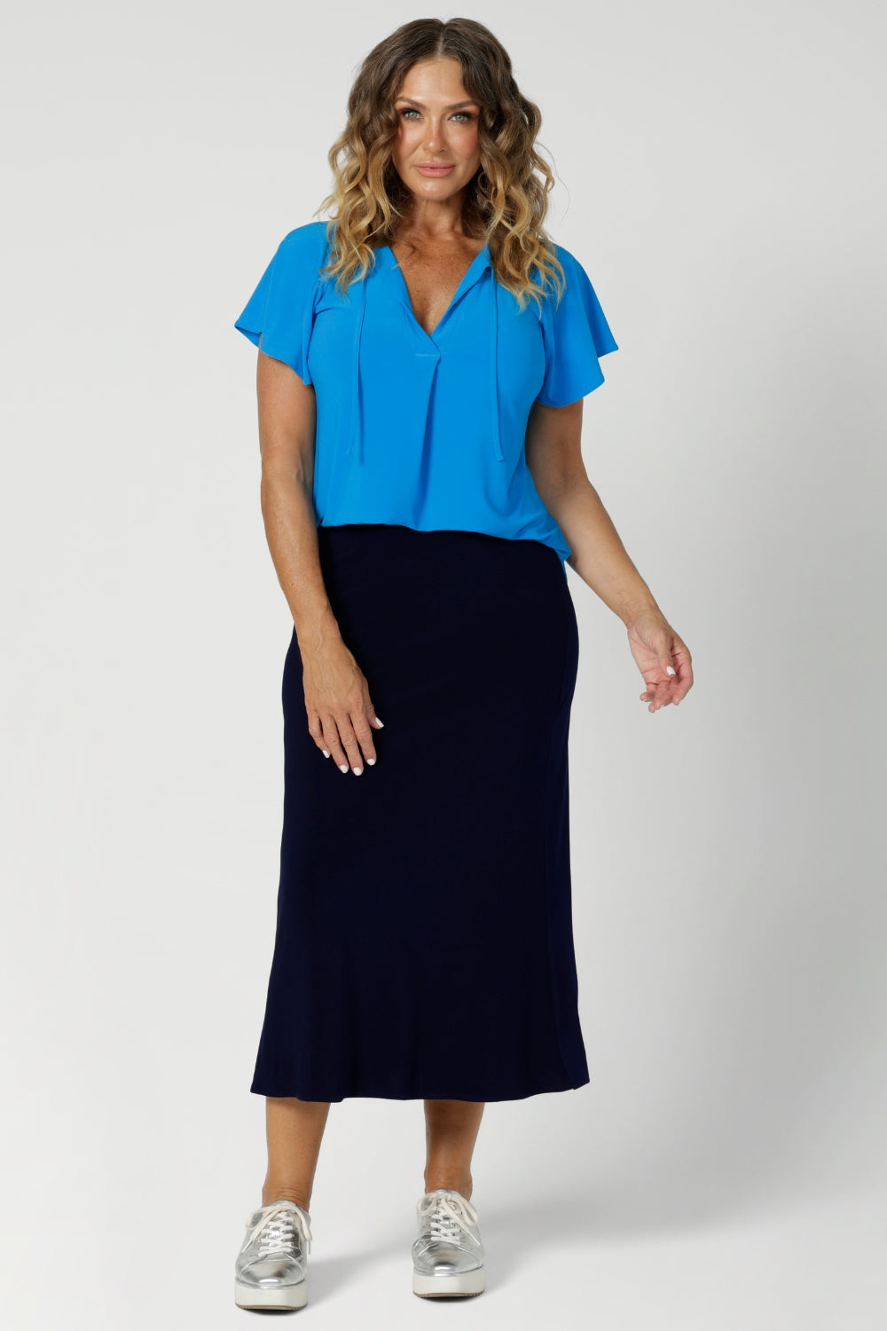 Flutter sleeve top worn by over 40's model features an easy, comfortable fit, while short flutter sleeves introduce a soft, feminine touch, creating a sense of movement with every wear. This workwear top also showcases a v neckline with neck ties that can be tied or left untied. 