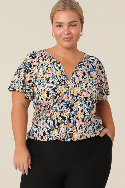 A plus size, size 14 woman wears a casual jersey top. The top has short raglan sleeves, a V-neckline and is printed with a floral pattern for a casual weekend look.