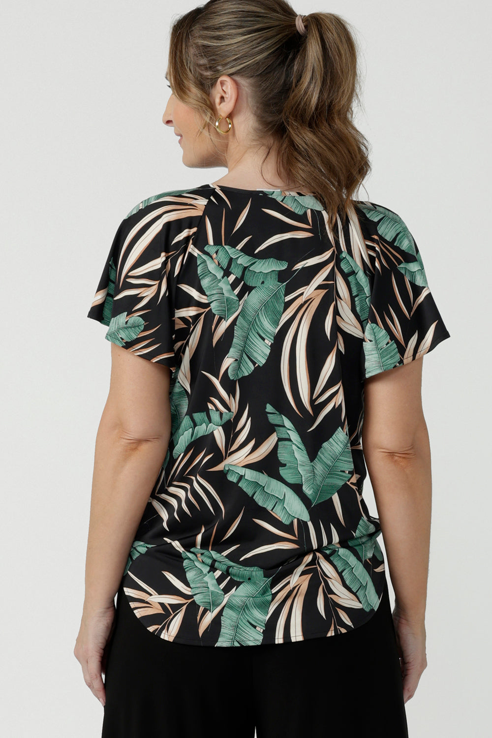 A flutter raglan sleeve jersey top with a flutter sleeve. Featuring a beautiful tropical print on a black background. Lightweight jersey cool to touch and easy care.