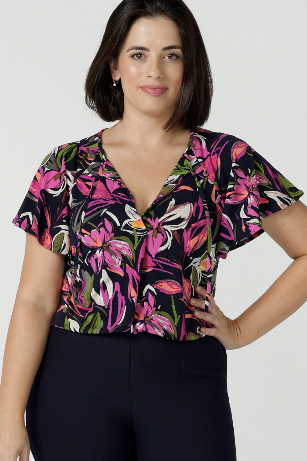 Size 10 woman wears the Bowie top in Vivid Flora with a raglan flutter sleeve, pleat front and v-neckline. Made in Australia for women size 8 - 24. 