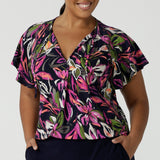 A size 16 woman wears the Bowie top in Vivid Flora with a raglan flutter sleeve, pleat front and v-neckline. Made in Australia for women size 8 - 24.