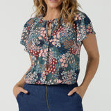 A size 10 woman wears the Bowie Top in jersey with flutter sleeves and tick neckline. Styled back with Denim Pants. Made in Australia for women size 8-24. 