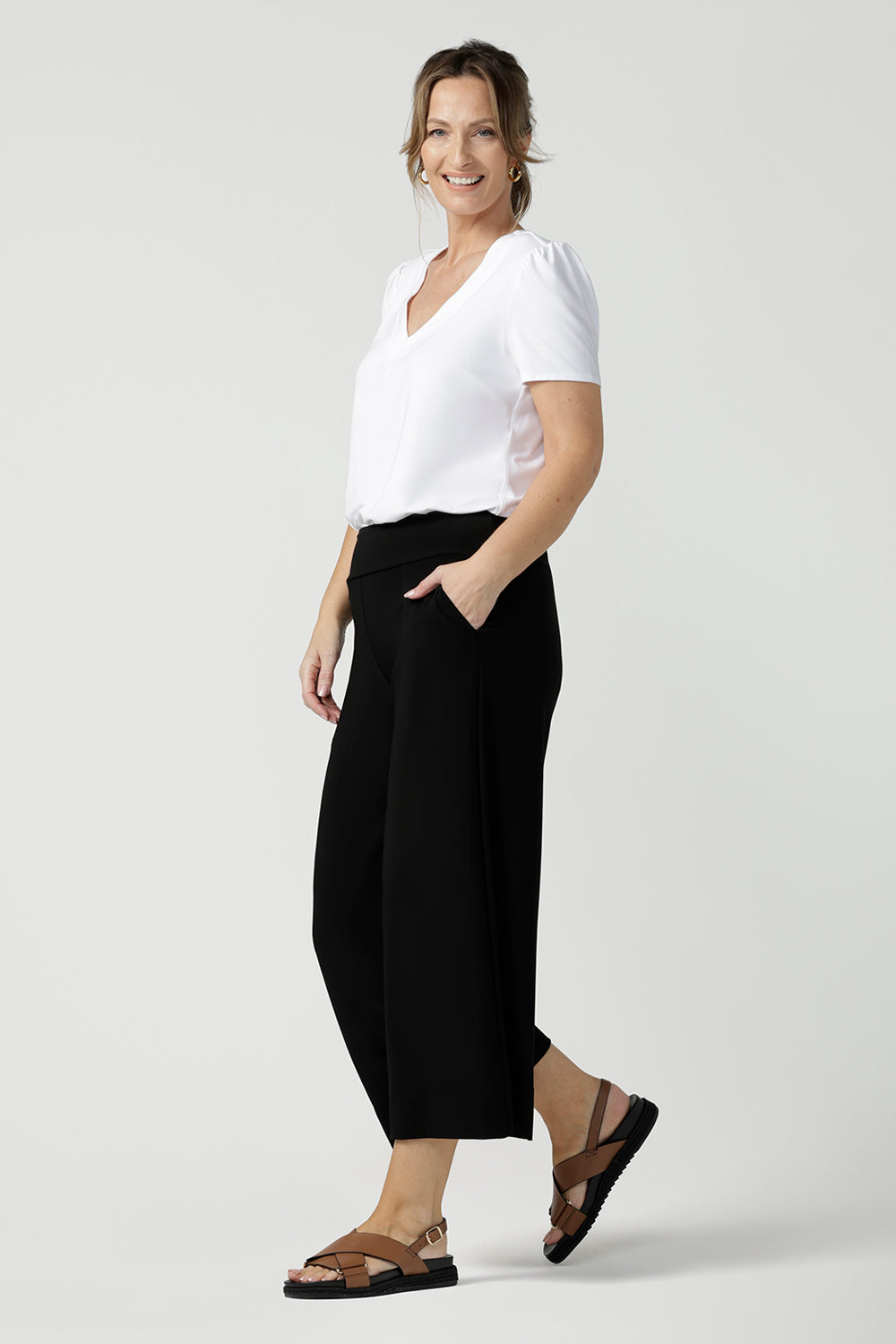 Side view of comfortable, wide leg black culotte pants worn with a V-neck white bamboo jersey top with short sleeves.. Cropped pants with pockets, these pull-on trousers are made in Australia by women's clothing brand, Leina & Fleur - size inclusive, shop online in petite, mid size and plus sizes.