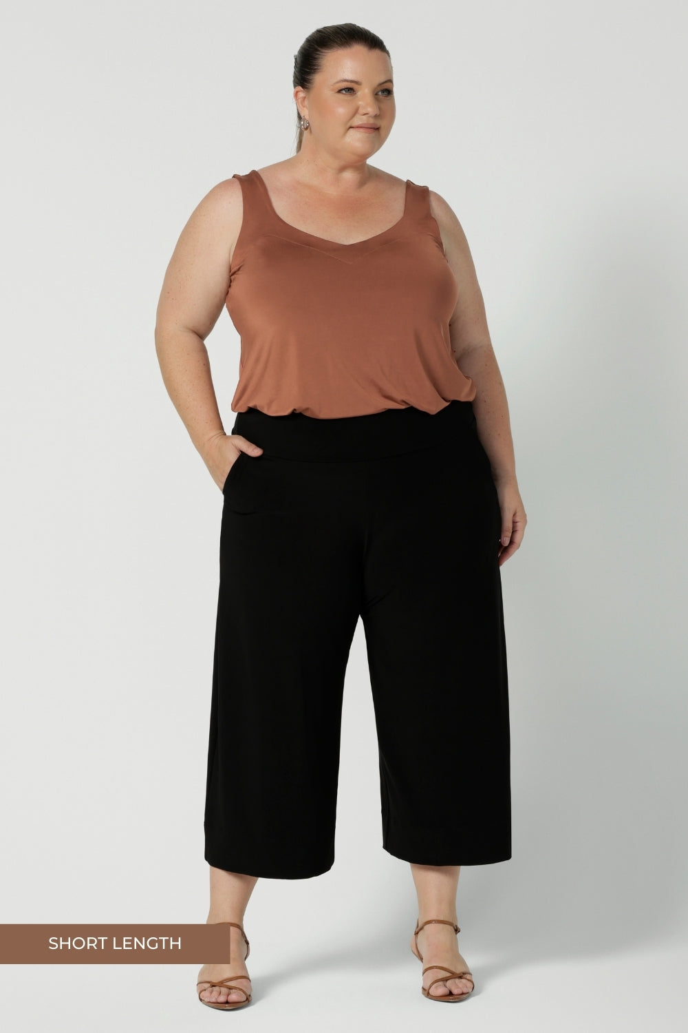 Plus sized woman wears wide leg black culotte pants. These cropped, short height  pants with pockets are a pull-on style, made in Australia by women's clothing brand Leina & Fleur. These workwear pants are size inclusive and are a considered design for woman in sizes 8-24.