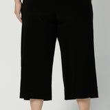 Back view of comfortable, wide leg black culotte pants are worn by a plus size, size 18 woman. Shorter cropped pants with pockets, these pull-on trousers are made in Australia by women's clothing brand, Leina & Fleur in sizes 8-24.