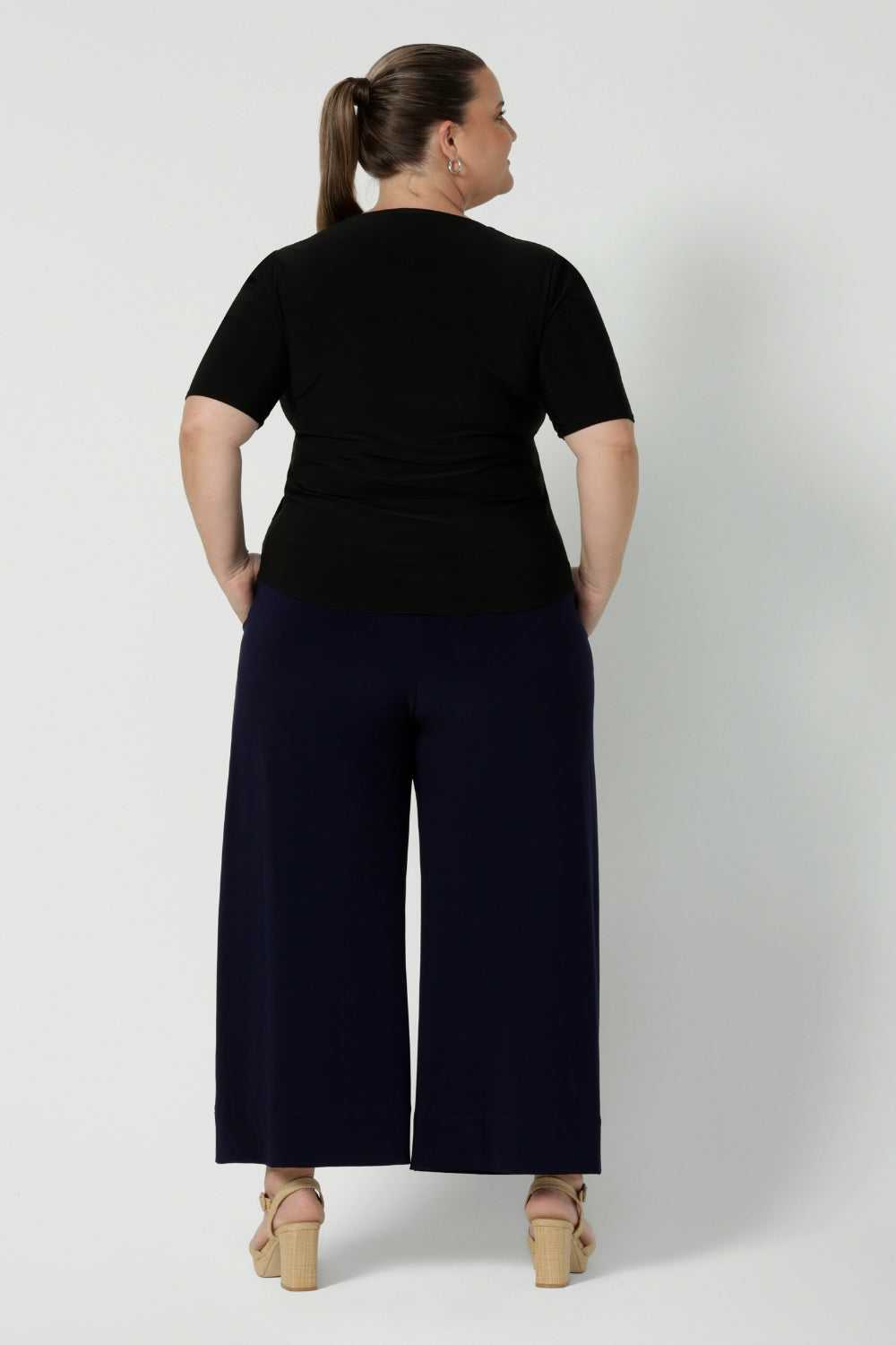 Plus size woman wears back-to-work pants that feature wide leg, pull on style in a deep navy colour. Australian made clothing brand Leina & Fleur stock these workwear pants in both regular & short lengths, considering tall and petite height women. Available in sizes 8-24.