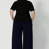 Plus size woman wears back-to-work pants that feature wide leg, pull on style in a deep navy colour. Australian made clothing brand Leina & Fleur stock these workwear pants in both regular & short lengths, considering tall and petite height women. Available in sizes 8-24.