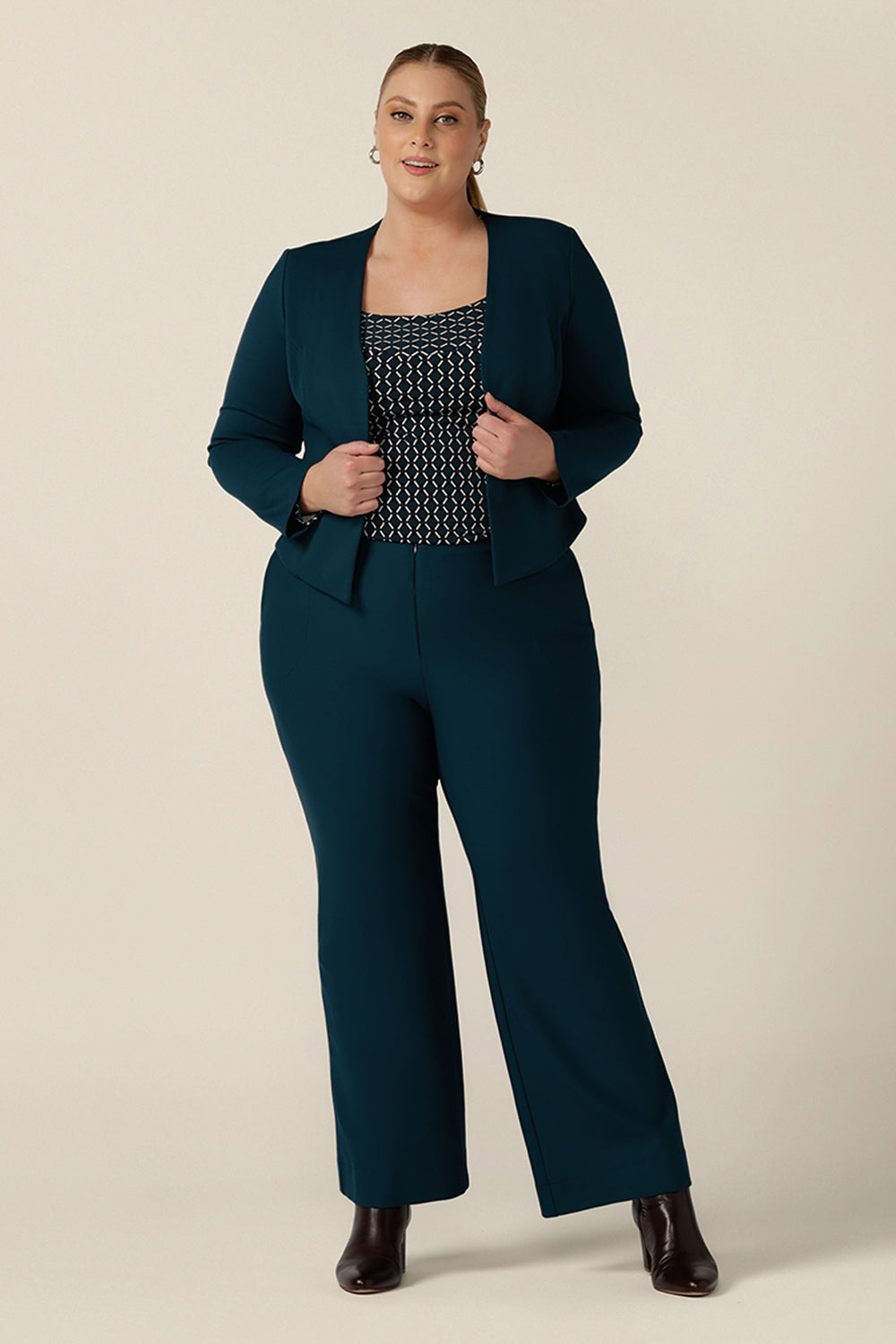 A plus size, size 18 woman wears a long sleeve top with squared scoop neckline. Worn with petrol blue, bootcut tailored pants and tailored blue work jacket, the geometric print jersey top is comfortable for corporate wear capsule wardrobes. Made in Australia, shop tops in sizes 8 to 24.