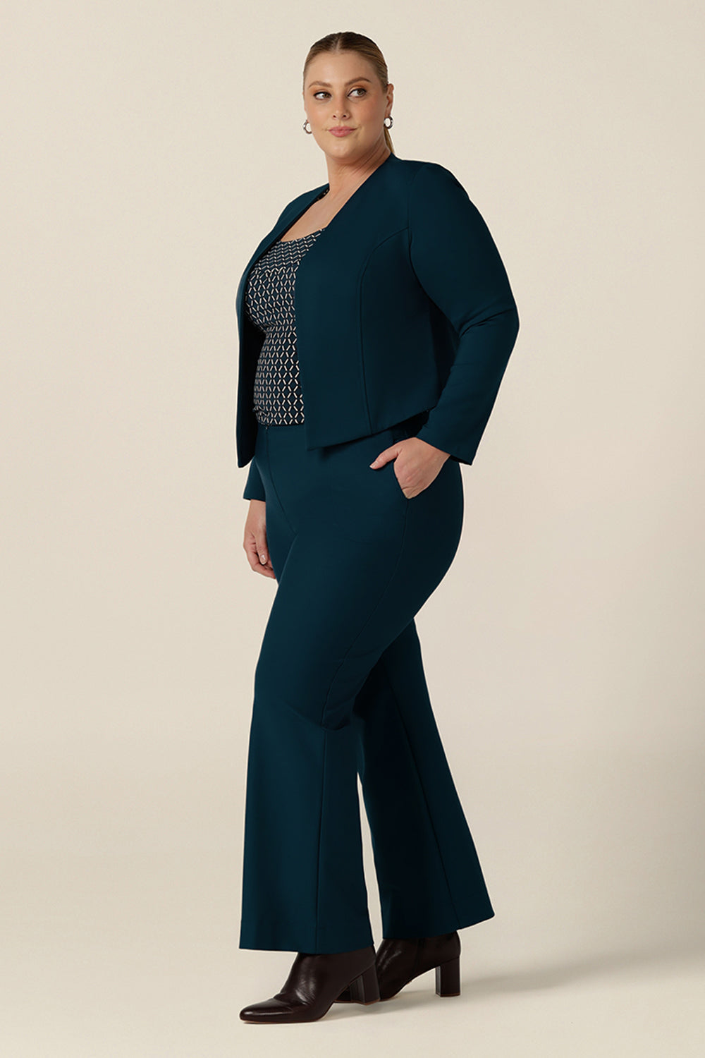 A plus size, size 18 woman wears petrol blue, tailored bootcut pants with a long sleeve printed top and tailored work jacket. Made in Australia in ponte fabric, these comfortable work pants are great for curvy women - shop in sizes 8 to 24.