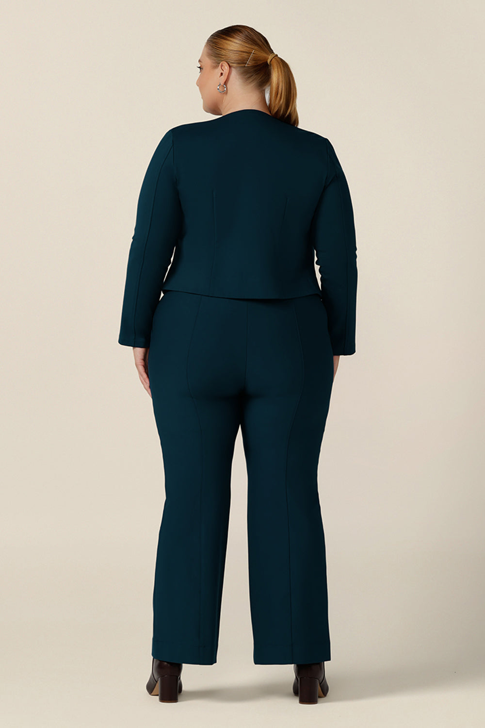 Back view of a plus size, size 18 woman wearing petrol blue, tailored bootcut pants with a long sleeve printed top and tailored work jacket. Made in Australia in ponte fabric, these comfortable work pants are great for curvy women - shop in sizes 8 to 24.