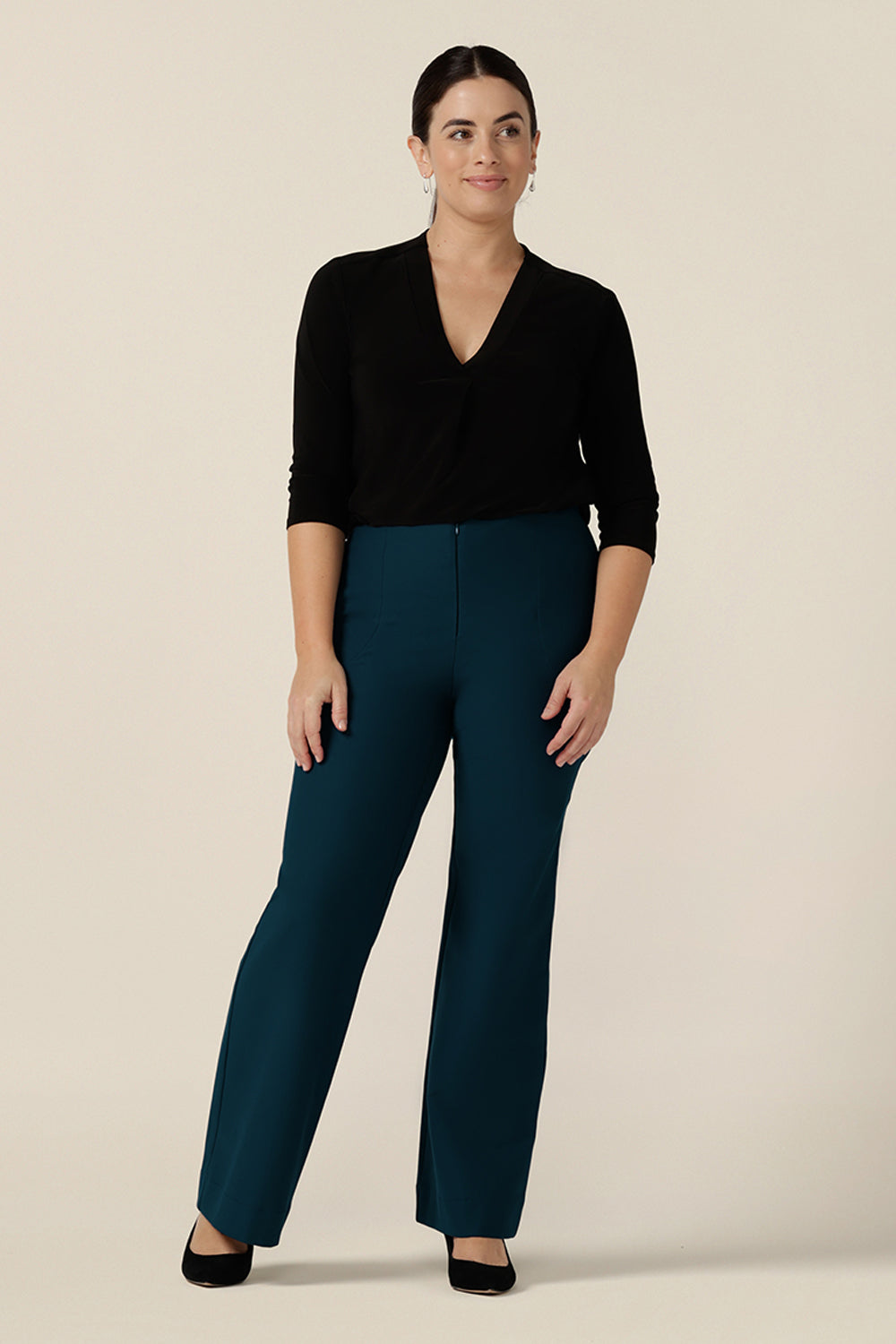 A size 10 woman wears petrol blue, tailored bootcut pants with a long sleeve black jersey top for an office wear look. Made in Australia in ponte fabric, these comfortable work pants are great for curvy women - shop in sizes 8 to 24.