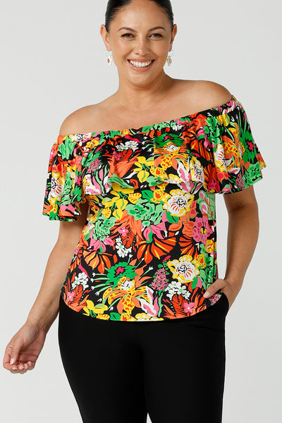 A size 12 woman wears and off shoulder ruffle Briar top in the Cancun print.  A bright and colourful pop of green, pink, orange and yellow floral print. A versatile top for the summer season, wear this top 3 ways. Designed and made in Australia sizes 8-24.