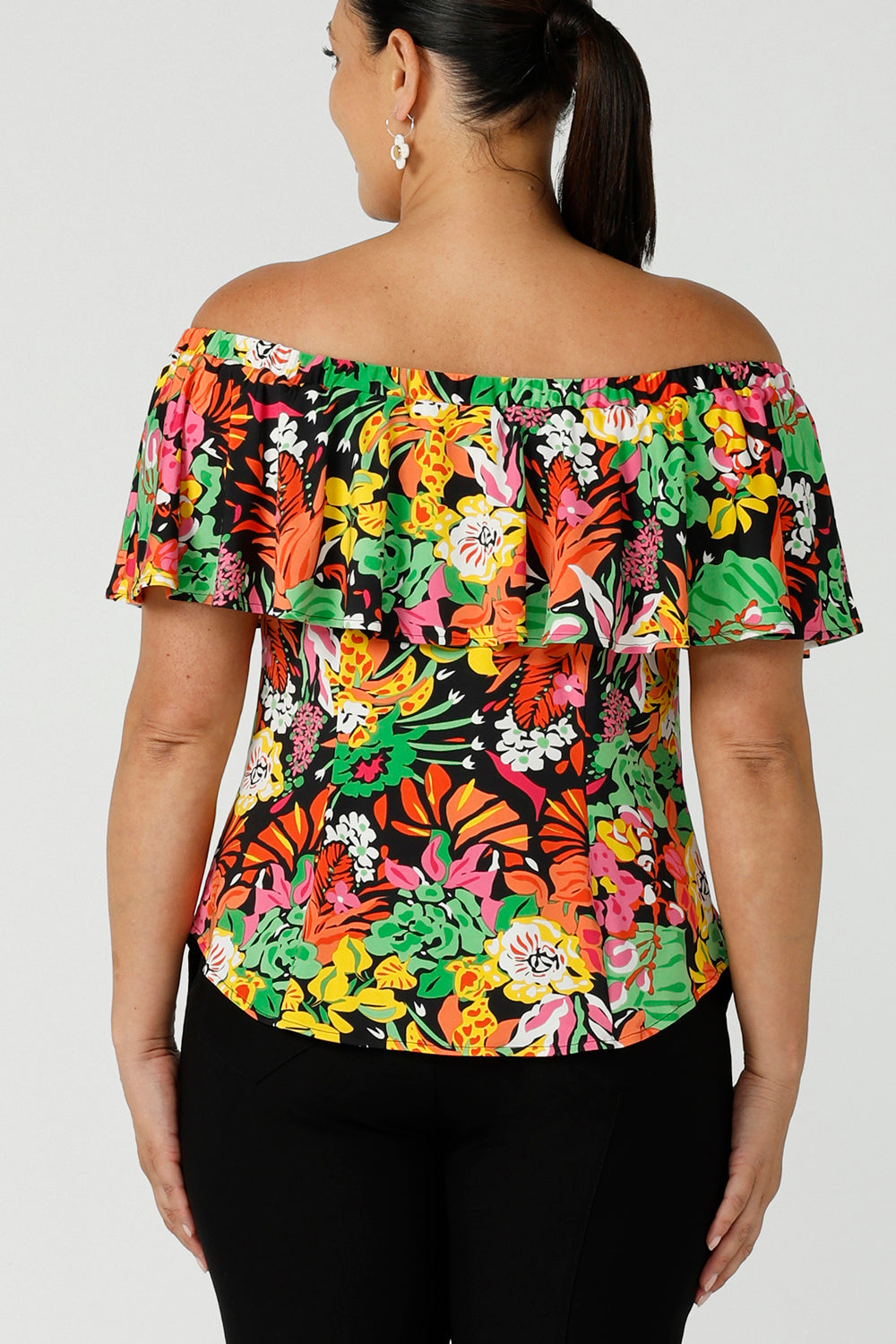 Back view of a size 12 woman wears and off shoulder ruffle Briar top in the Cancun print. A bright and colourful pop of green, pink, orange and yellow floral print. A versatile top for the summer season, wear this top 3 ways. Designed and made in Australia sizes 8-24.