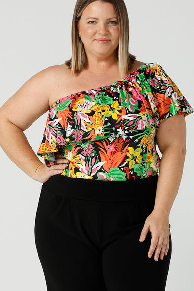 Close up of curvy woman wears a size 18 off shoulder ruffle Briar top in the Cancun print. A bright and colourful pop of green, pink, orange and yellow floral print. Styled back with black work pants. A versatile top for the summer season, wear this top 3 ways. Designed and made in Australia sizes 8-24.