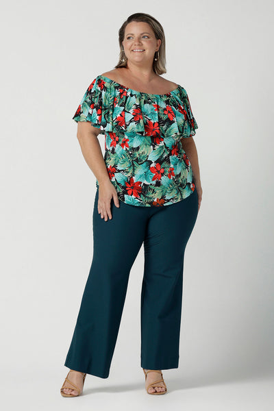 Off shoulder Briar Top in Havana on a size 18 model. Tropical print design with red flowers and green palm leaf. Soft slinky jersey. Wear this top multiple ways one shoulder, off shoulder and on shoulder. Styled back with Brett pants in Petrol.  Made in Australia for women size 8 - 24.