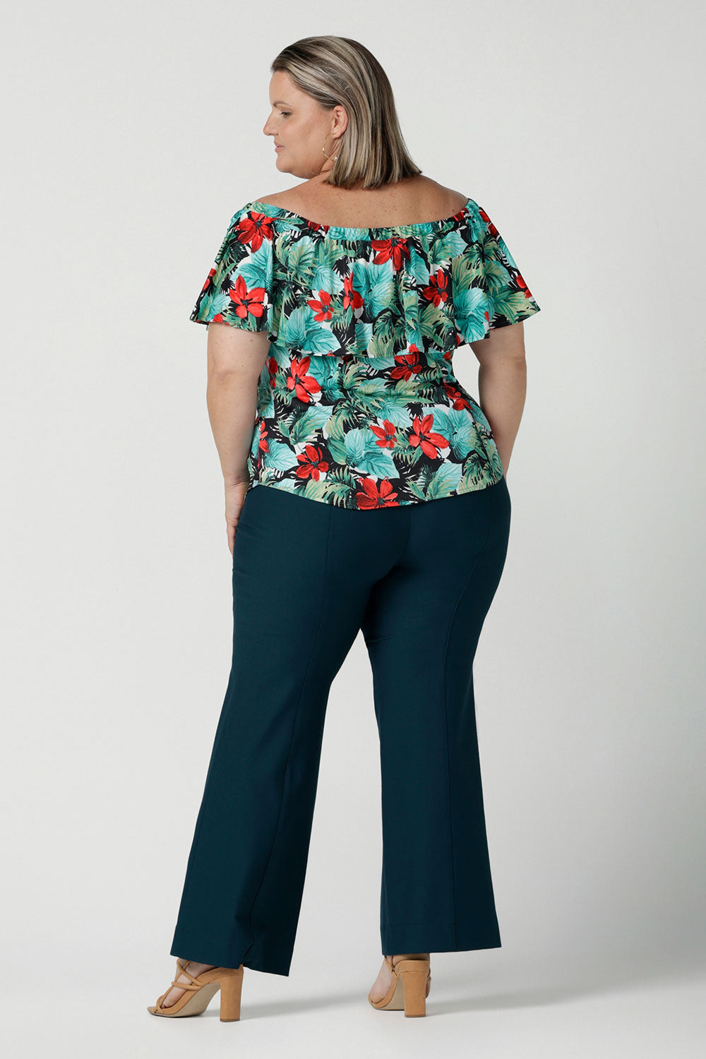 Back view of off shoulder Briar Top in Havana on a size 18 model. Tropical print design with red flowers and green palm leaf. Soft slinky jersey. Wear this top multiple ways one shoulder, off shoulder and on shoulder. Styled back with Brett pants in Petrol. Made in Australia for women size 8 - 24.