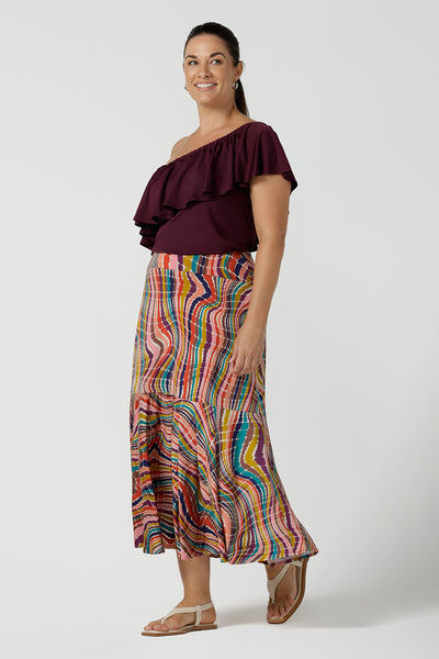 Curvy size 12 woman wears the Briar Top in Plum. A off shoulder style that can be worn in multiple ways. Wear it off or on shoulder. Deep mulberry plum colour is soft slinky jersey with ruffle frill. Styled back with Berit skirt in Kaleidoscope rainbow. Made in Australia for women size 8 - 24.