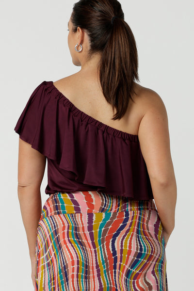 Back view of Curvy size 12 woman wears the Briar Top in Plum. A off shoulder style that can be worn in multiple ways. Wear it off or on shoulder. Deep mulberry plum colour is soft slinky jersey with ruffle frill. Made in Australia for women size 8 - 24.