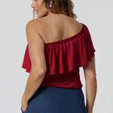 Back view of 40 year old model wears red off the shoulder top. Top has been styled under the shoulders paired back with our Vintage Denim Dutton Pants. Made to drape beautifully with red slinky jersey fabric. The red colour makes it perfect for any season, adding a bold pop of colour. Australian made quality, this easy care top allows you to express your unique style. Retail label Leina and Fleur proudly stocks plus and petite sizes ranging from 8 to 24.