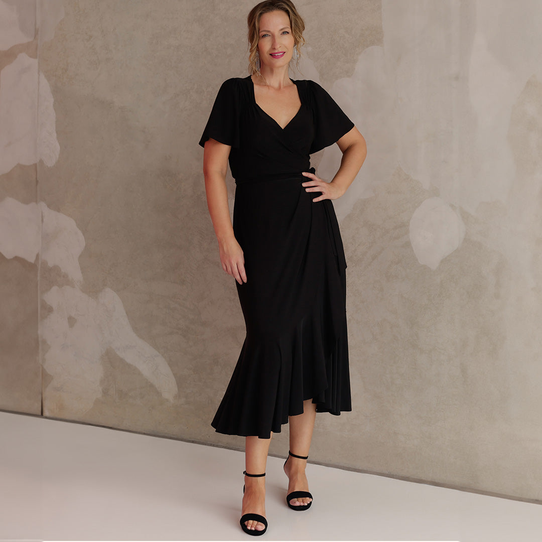 Showing good black dresses for women in Australia and New Zealand, an over 40, size 10 woman wears a black maxi length wrap dress with flutter sleeves. Made in Australia by women's dress brand, Leina & Fleur, this black cocktail dress is a great dress for curvy, mid size and petite women's evening wear and occasionwear.