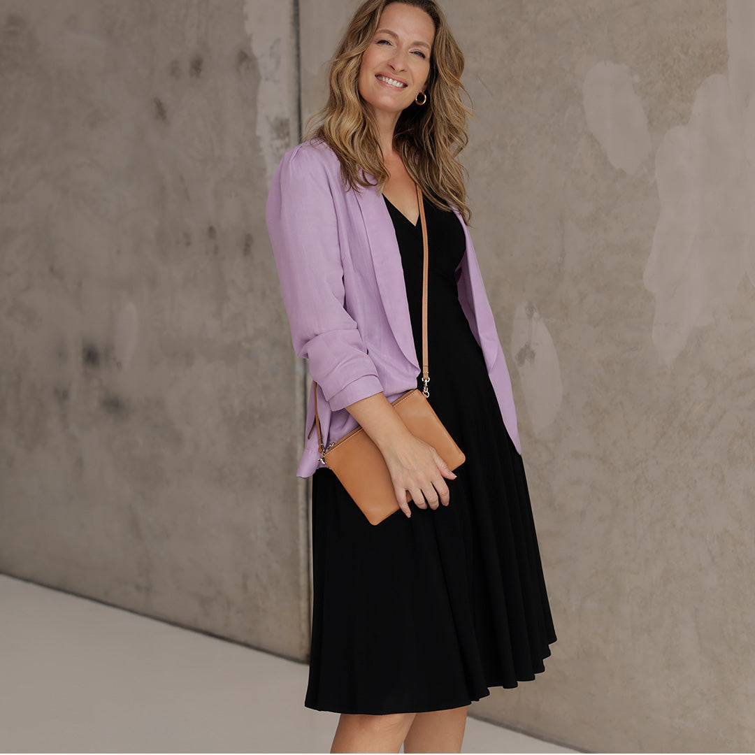 Wearing a black fixed wrap dress with midi length hemline styled with a lilac longline blazer in eco-conscious Tencel fabric, a size 10, over 40 woman shows how versatile black dresses wear for every day, casual and weekend style. Both made in Australia by women's clothing brand Leina & Fleur, shop both women's dresses and jackets online in sizes 8 to 24.