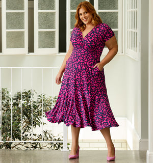 A size 18 plus size woman wears a fixed wrap jersey dress for Valentines Day date night. The dress has a V-neck, short sleeves and full knee-length skirt. Made from stretch jersey and produced in Australia, the dress features a pink heart print designed by L&F on the Gold Coast, Queensland, Australia