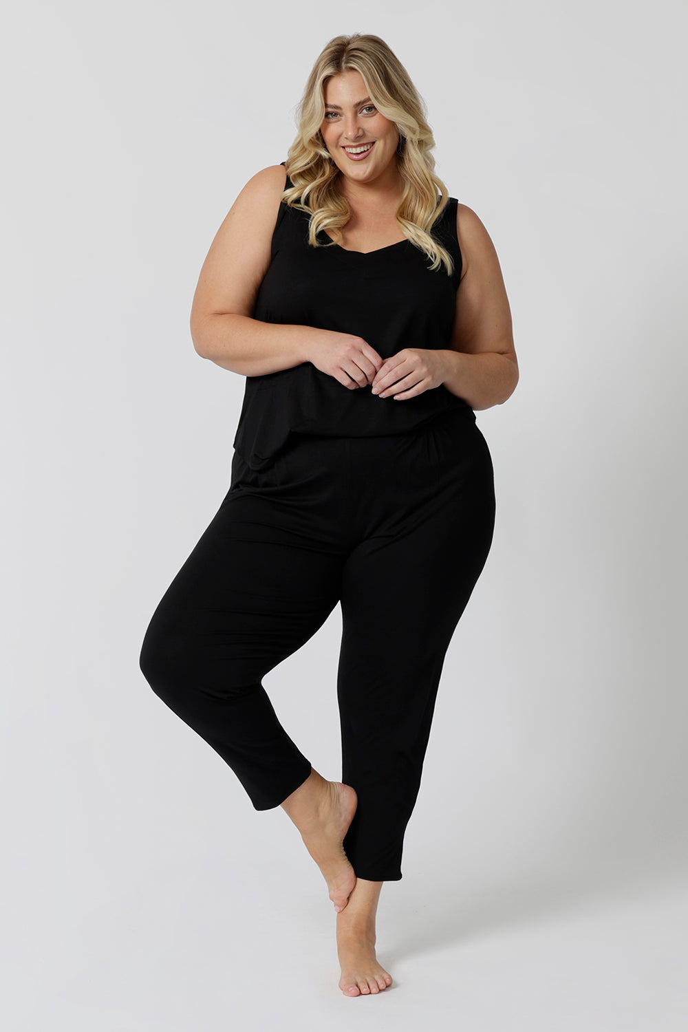 Showing a good loungewear cami top for curve women, a size 18 woman wears a plus size cami top in black bamboo jersey. Thermo-regulating this sleepwear top is a good top for menopause and night sweats. Cami top is Worn with tapered leg lounge pants. Shop lounge wear tops online in sizes 8-24.