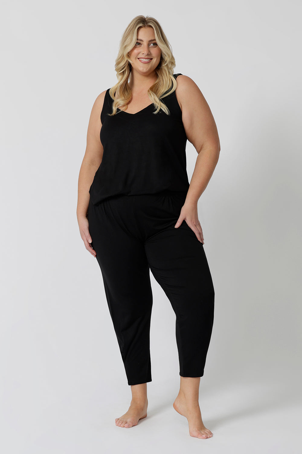 Showing a good lounge wear cami top for curve women, a size 18 woman wears a plus size cami top in black bamboo jersey. Thermo-regulating this sleeveless sleepwear top is a good top for menopause and night sweats. This black Cami top is Worn with tapered leg lounge pants. Shop lounge wear tops online in sizes 8-24.