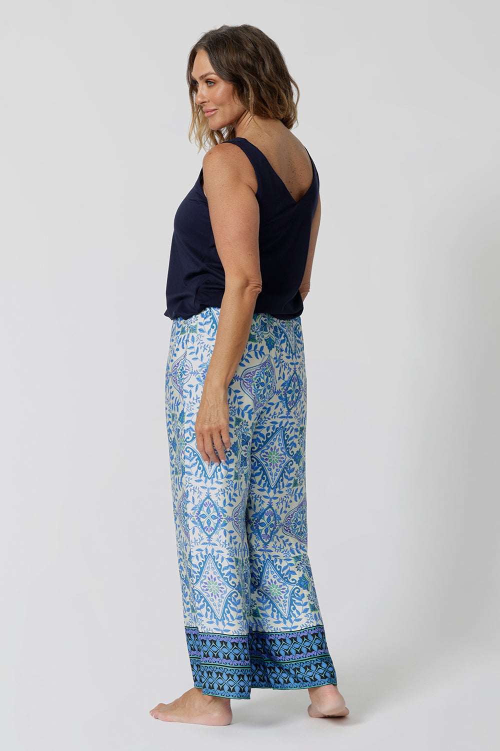 Back view of a pretty blue  pyjama set that's great for over 40s women. A size 12 woman wears straight leg pyjama pants with blue and white print and a navy blue bamboo jersey cami top with wide shoulder straps. Thermo-regulating and breathable, these pajama pants with drawstring ties are good pyjamas for night sweats and hot flushes. Shop this loungewear set online at L&F Australia in sizes 8 to 24.