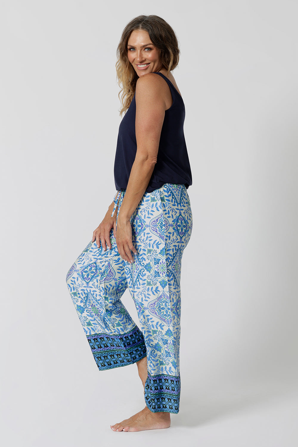 Side view of a pretty pyjama set that's great for over 40s women. A size 12 woman wears straight leg pyjama pants with blue and white print and a navy blue bamboo jersey cami top with wide shoulder straps. Thermo-regulating and breathable, these pajamas pants with drawstring ties and good pyjamas for night sweats and hot flushes. Shop loungewear sets online at L&F Australia in sizes 8 to 24.